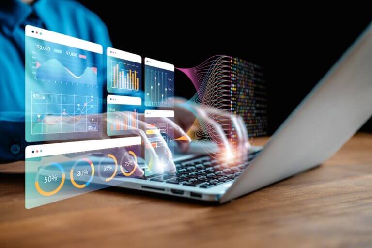 Manos usando una laptop con visualizaciones interactivas de Big Data que incluyen dashboards, gráficos de rendimiento y flujos de datos, representando el análisis en tiempo real para empresas.