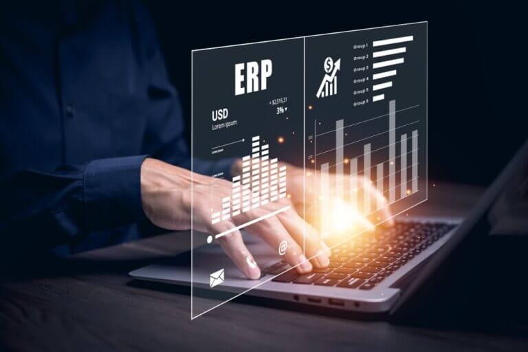 Ejecutivo trabajando en una laptop con gráficos y panel digital de ERP que muestran estadísticas financieras y de productividad, ilustrando los beneficios del ERP para empresas.