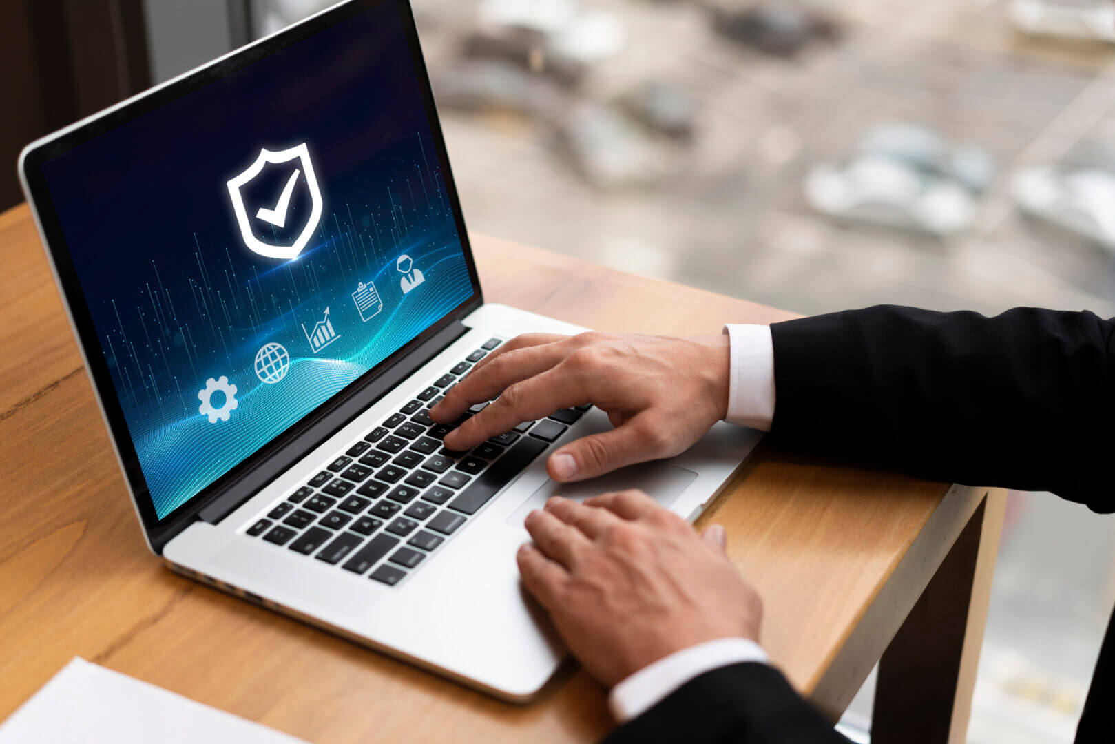 Persona utilizando un portátil con íconos de seguridad digital y un escudo en la pantalla, representando la importancia de proteger datos en el entorno corporativo.