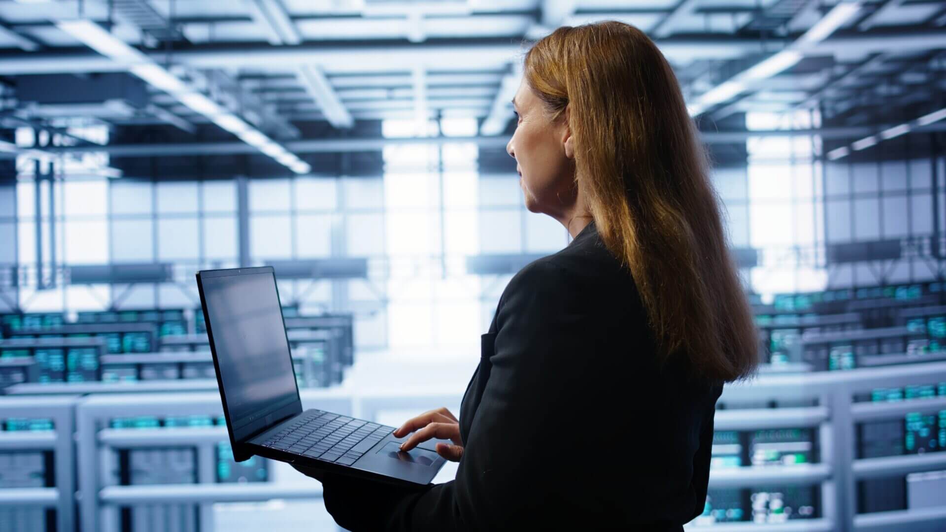 Profesional observando servidores y gestionando datos desde un portátil en un centro tecnológico, representando la supervisión de Big Data empresarial.