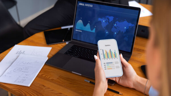 Profesional revisa en laptop y móvil un panel de datos para machine learning en finanzas, con gráficos de mercado global.