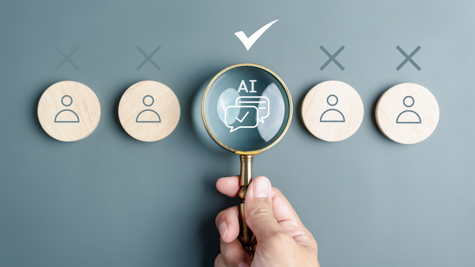 Imagen de una mano sosteniendo una lupa sobre un token central que dice "AI" con burbujas de diálogo y una marca de verificación. Otros cuatro tokens con iconos de usuario tienen una 'X' encima de ellos, simbolizando la AI como la opción elegida frente al talento humano tradicional en los despidos tecnológicos de 2026.