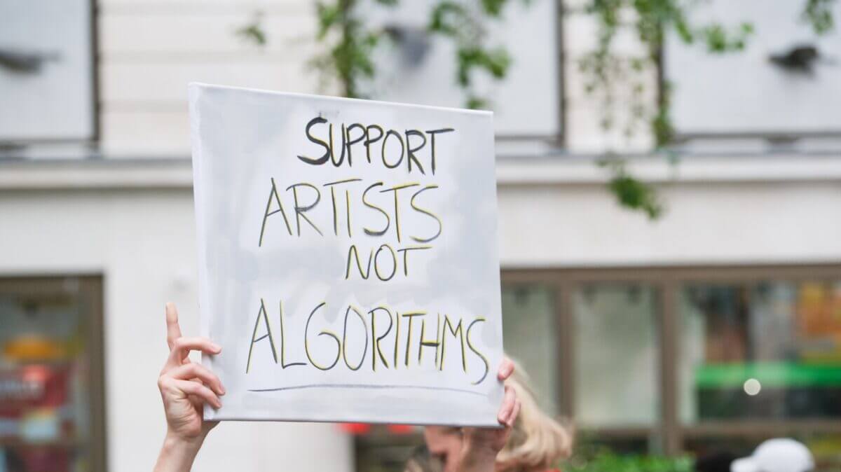 Pancarta de protesta con el texto en inglés "Support Artists Not Algorithms" sostenida en una manifestación pública para defender los derechos de autor frente a la AI.