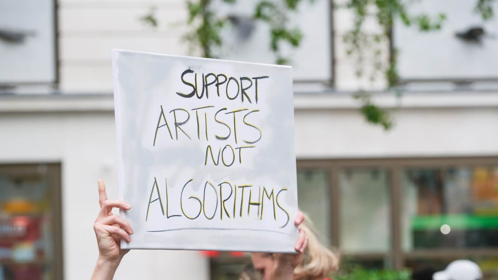 Pancarta de protesta con el texto en inglés "Support Artists Not Algorithms" sostenida en una manifestación pública para defender los derechos de autor frente a la AI.