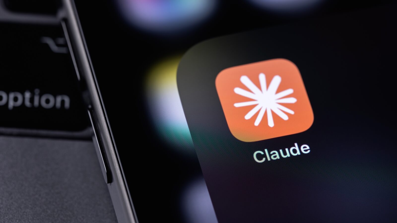Icono de la aplicación Claude de Anthropic en la pantalla de un smartphone sobre el teclado de un ordenador.
