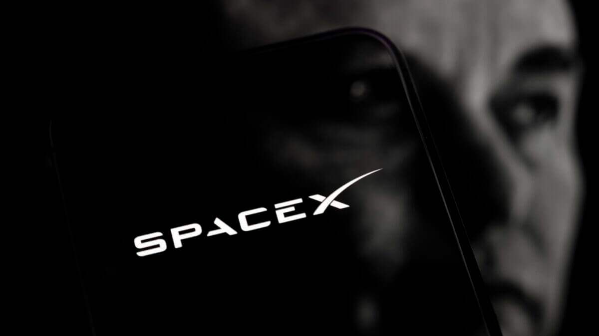 Logo de SpaceX en smartphone sobre rostro de Elon Musk, ilustrando la SpaceX alianza Nvidia AI.