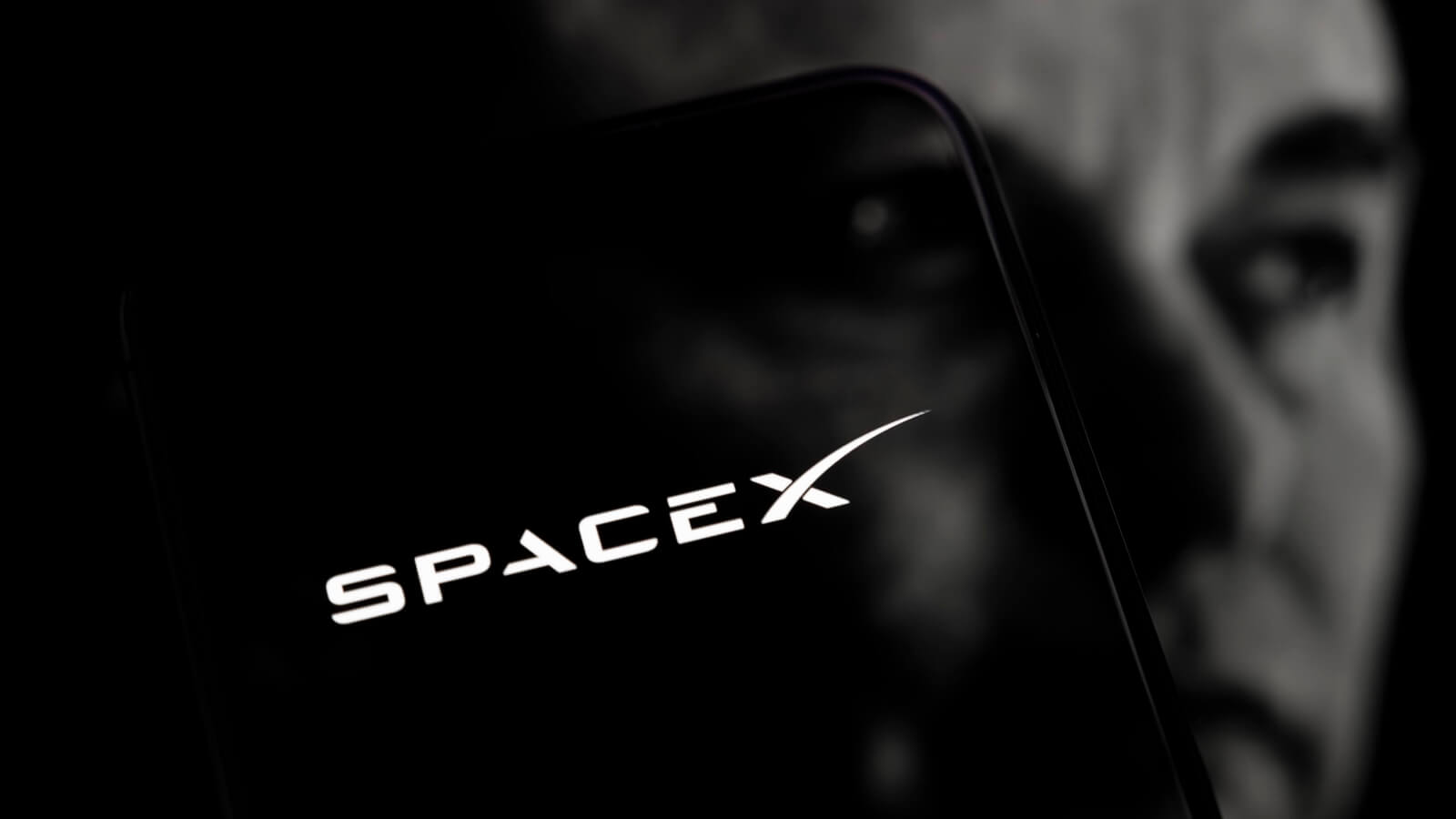 Logo de SpaceX en smartphone sobre rostro de Elon Musk, ilustrando la SpaceX alianza Nvidia AI.