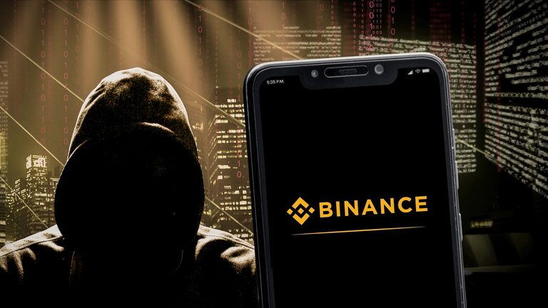 Hacker encapuchado junto a un smartphone con la aplicación de Binance, representando un ciberataque a Binance.