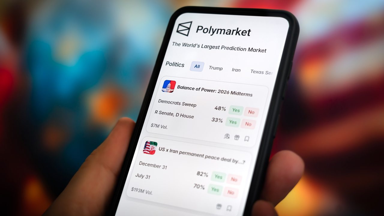 Persona sosteniendo un smartphone que muestra la pantalla principal de la plataforma de predicciones Polymarket.